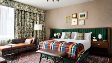 Una habitación de hotel con una cama grande, un banco, un sofá y una mesita de noche.
