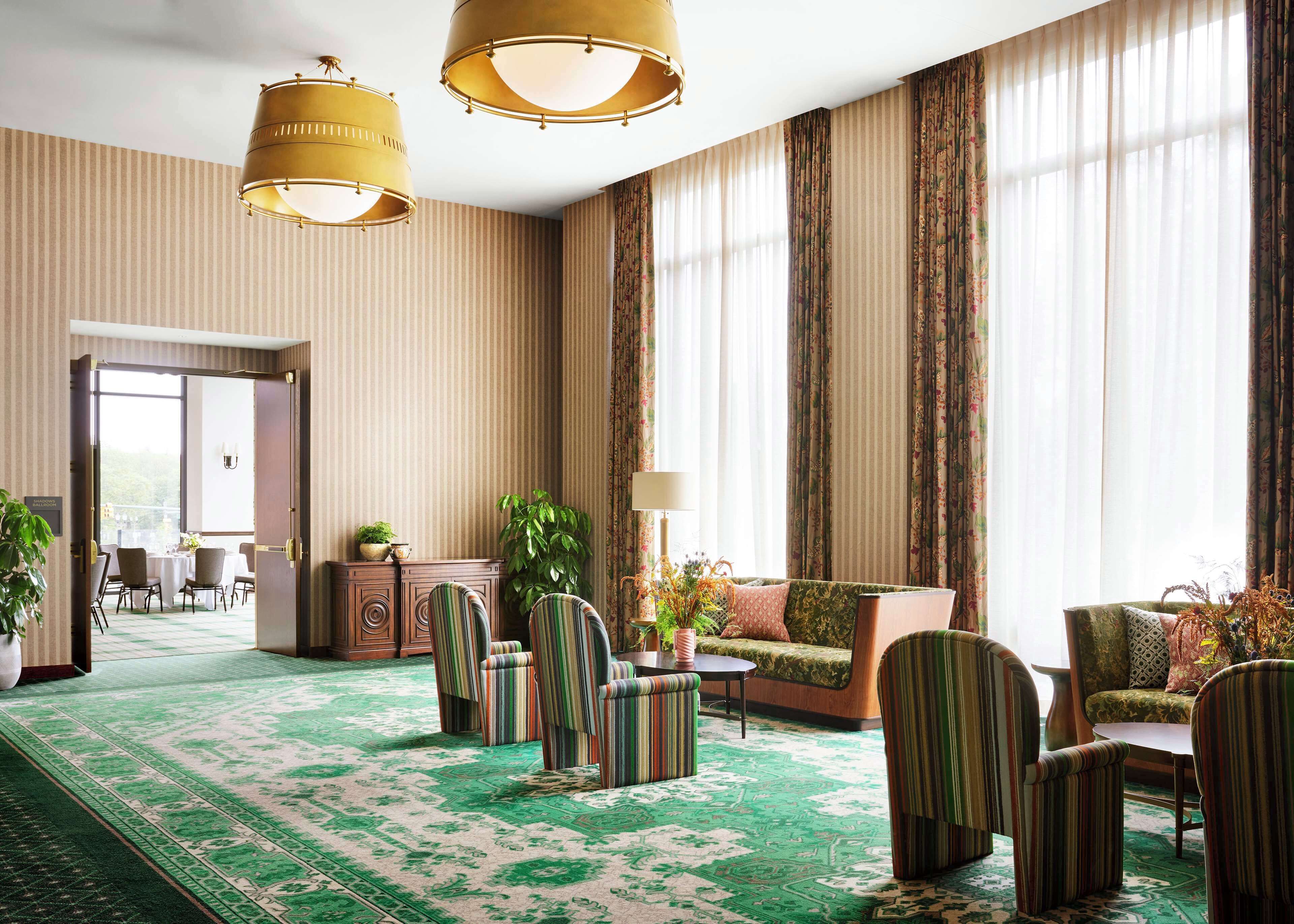 Un vestíbul d'hotel espaiós amb paper pintat a ratlles, una catifes estampada de verd i una zona de seients amb butaques i un sofà a ratlles.
