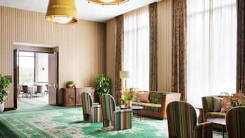 Un vestíbul d'hotel espaiós amb paper pintat a ratlles, una catifes estampada de verd i una zona de seients amb butaques i un sofà a ratlles.