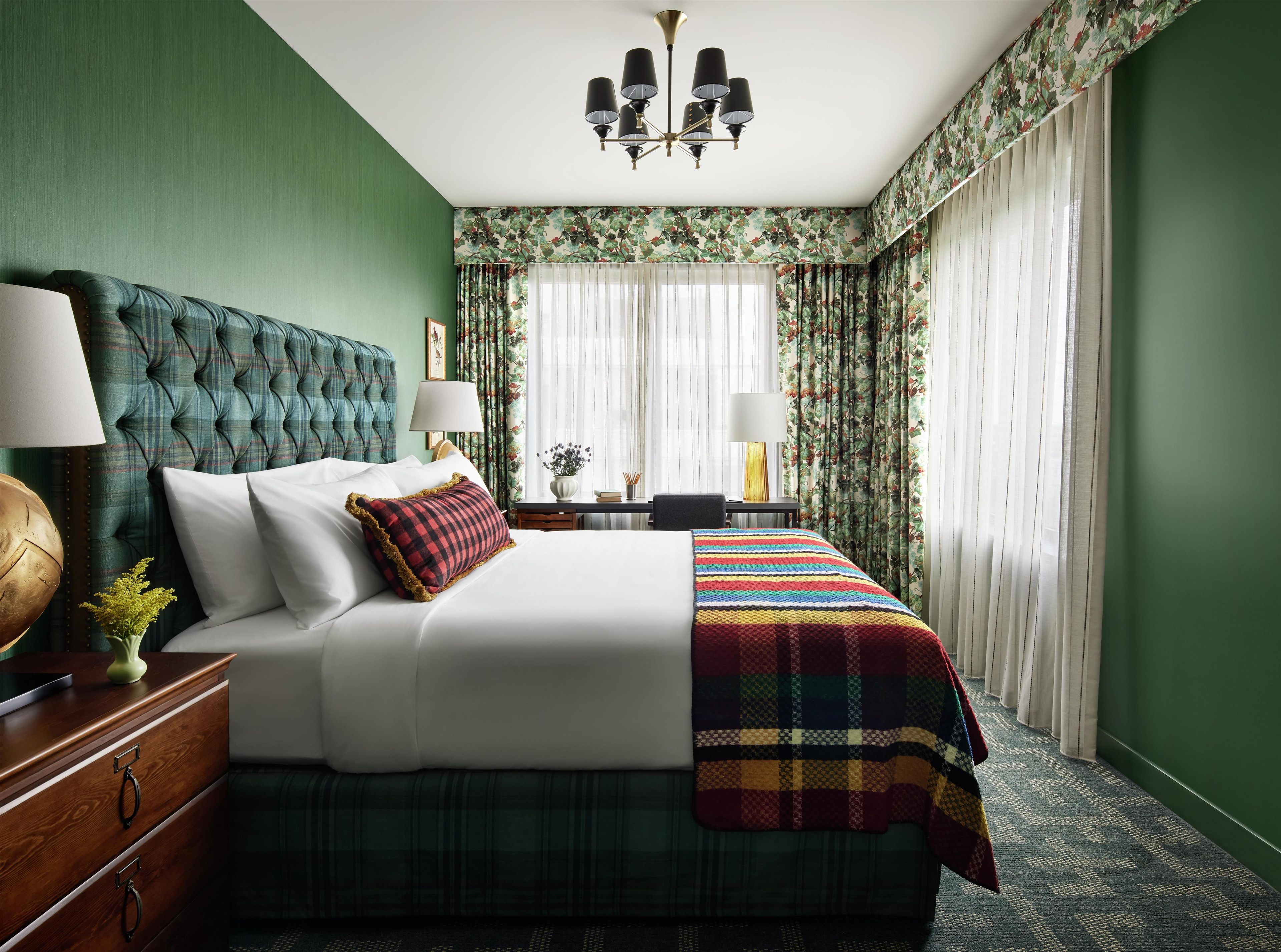 A hotel room with a large bed, two bedside lamps, a chandelier, and floral wallpaper.