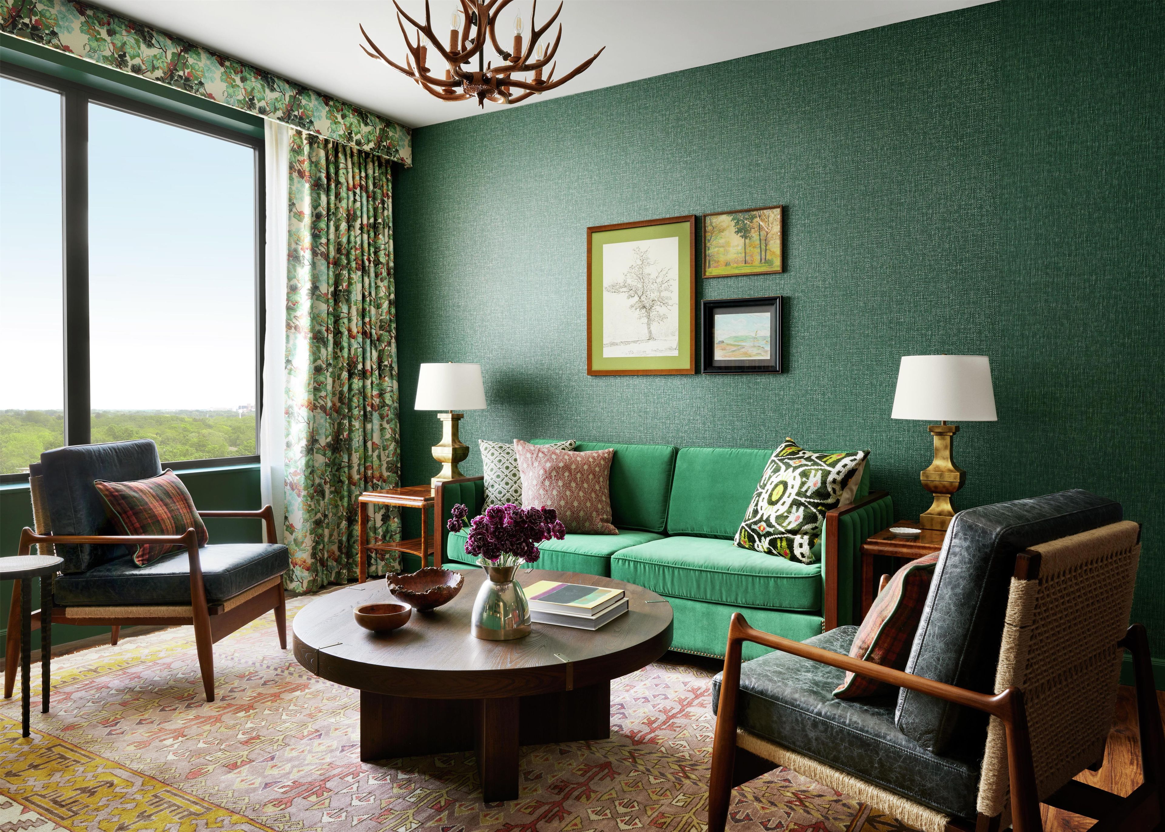 A room with a green wall, a green sofa, a round coffee table, and two lamps.