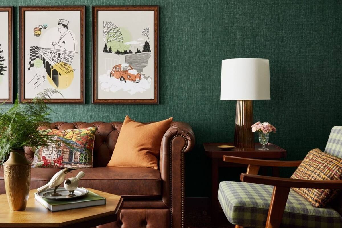 Un salon chaleureux avec un canapé en cuir marron, une table basse en bois sur laquelle reposent un livre et une statuette d’oiseau, une table d’appoint avec une lampe, et des œuvres d’art encadrées accrochées au mur.