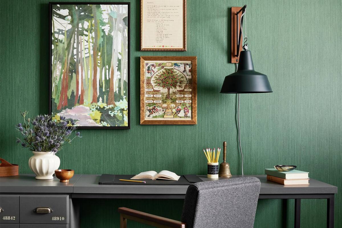 Un bureau moderne, avec une chaise, une lampe et des œuvres d’art encadrées, le tout placé devant un mur vert.