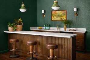 A kitchen with a wooden bar, stools, a sink, and a green textured wall.