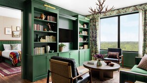 Una sala de estar acogedora con un sofá verde, una mesa de centro redonda, una estantería y un ventanal con vistas al exterior.