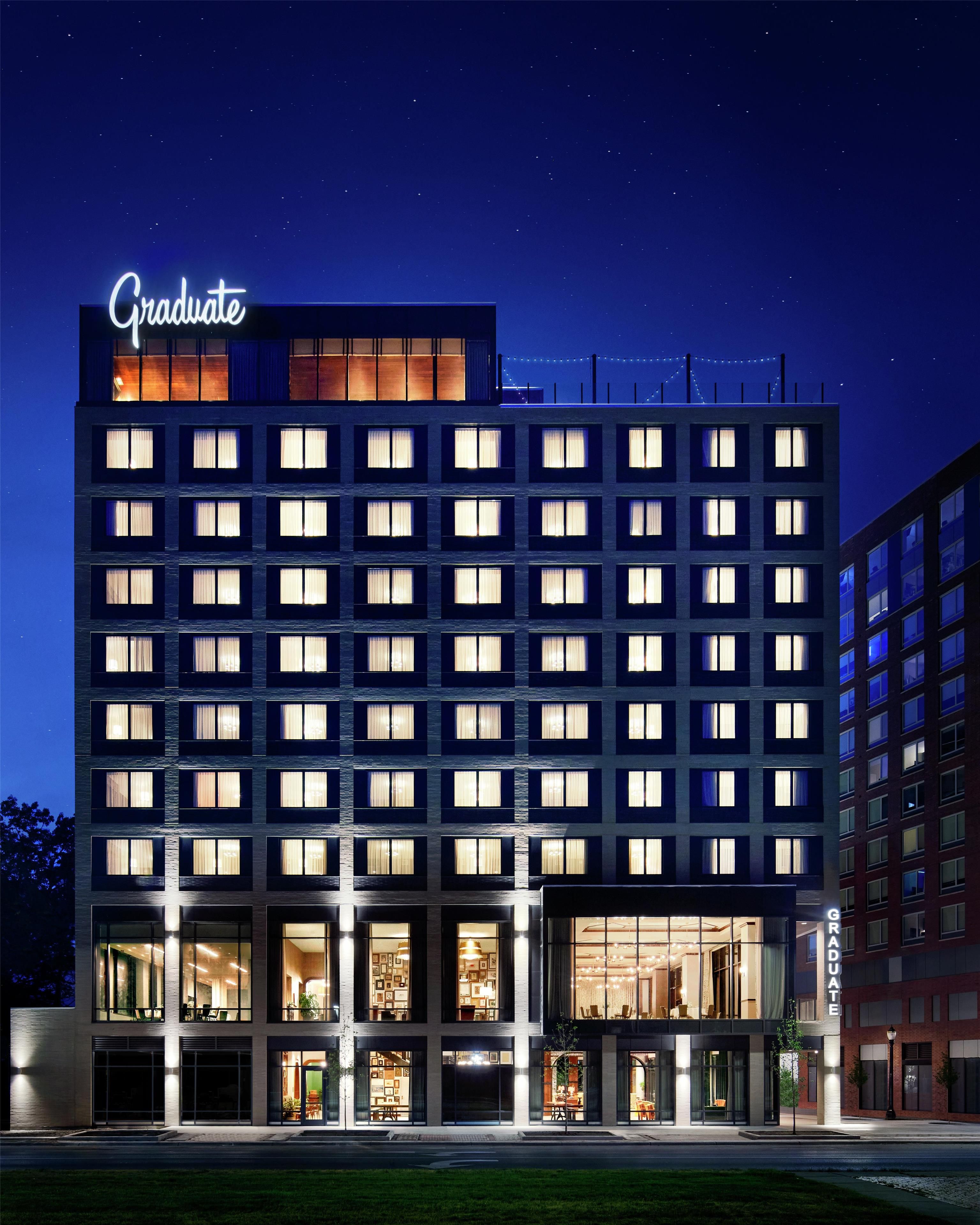 A multi-story hotel with a prominent "Graduate" sign, large windows, and a well-lit facade.