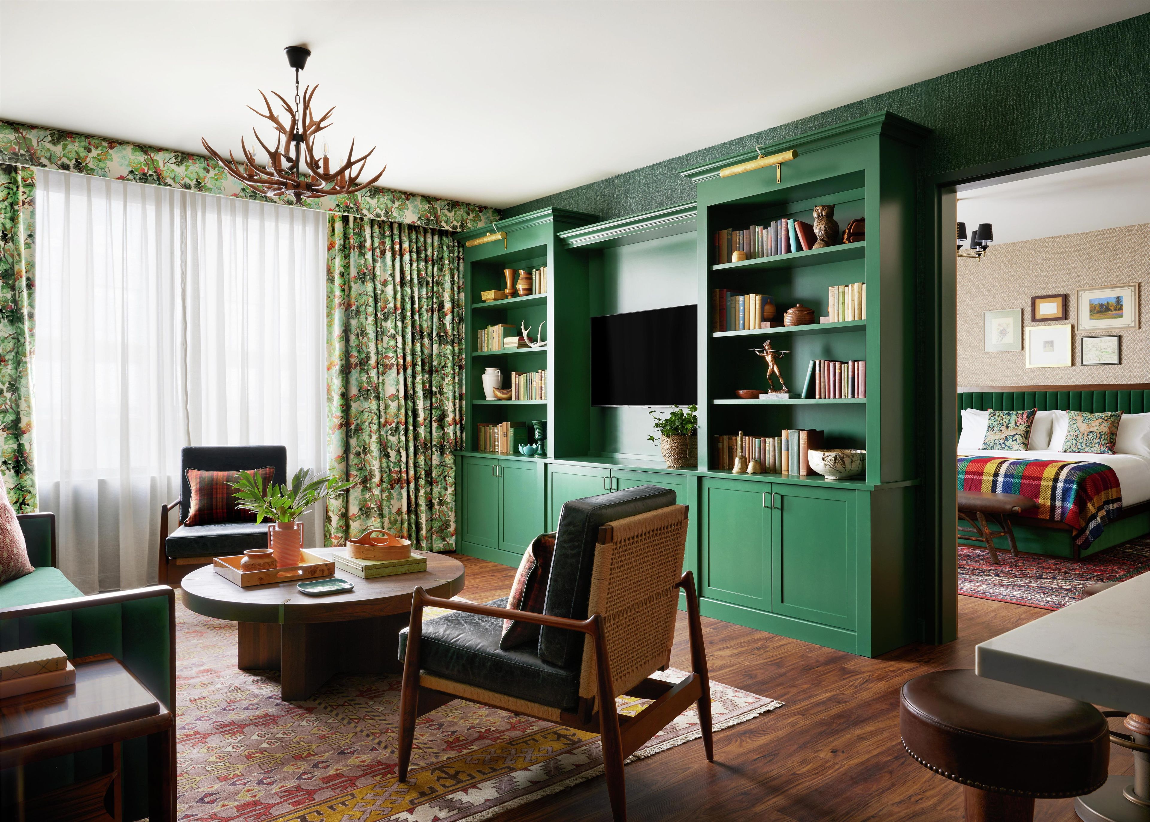 Una habitación con una estantería verde, una mesa de centro redonda, un sofá, una mesa de comedor y una alfombra estampada.
