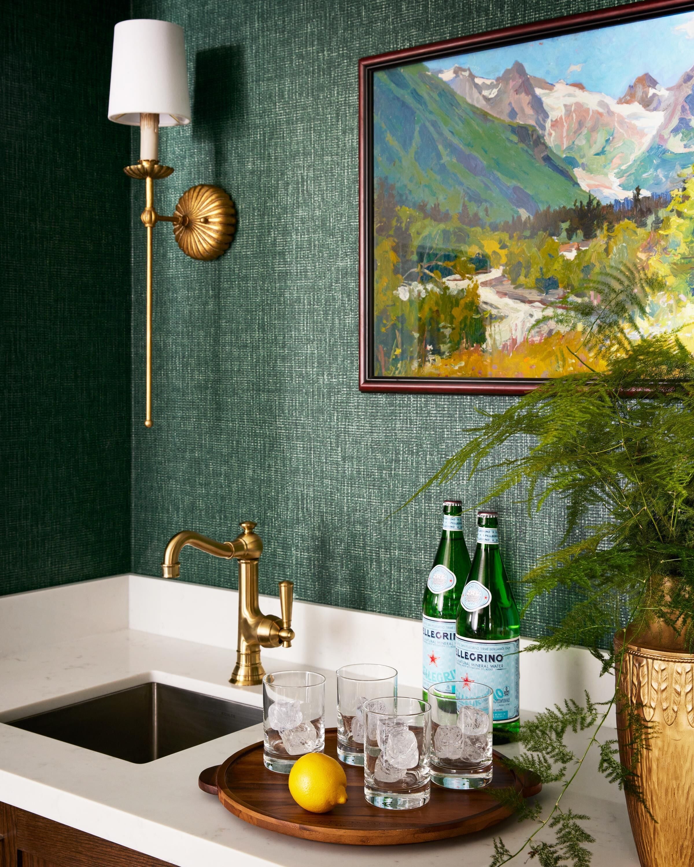 A bathroom with a sink, a gold faucet, a green bottle, and a framed painting on the wall.