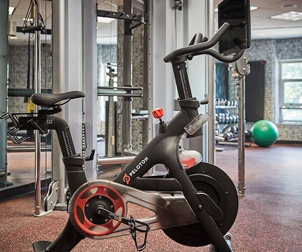 A stationary bike in a gym with a weight bench and a green exercise ball in the background.