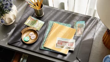A desk with a notebook, postcards, a pen holder, and a small bowl with a label.