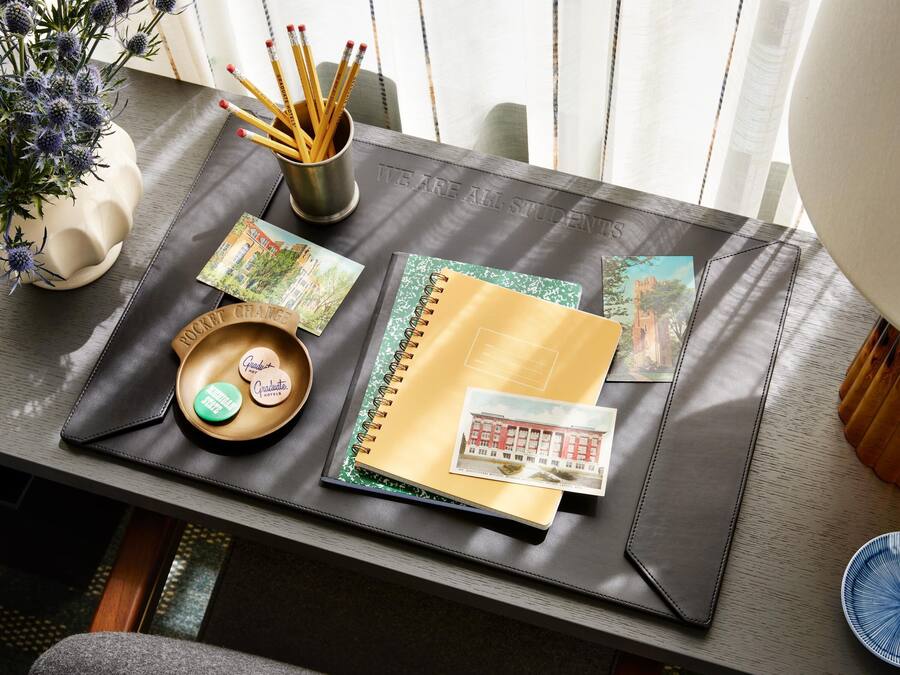 A desk with a notebook, postcards, a pen holder, and a small bowl with a label.