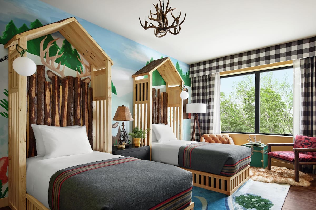 Une chambre avec deux lits, une fenêtre donnant sur un beau paysage, un lustre et un rideau à carreaux.