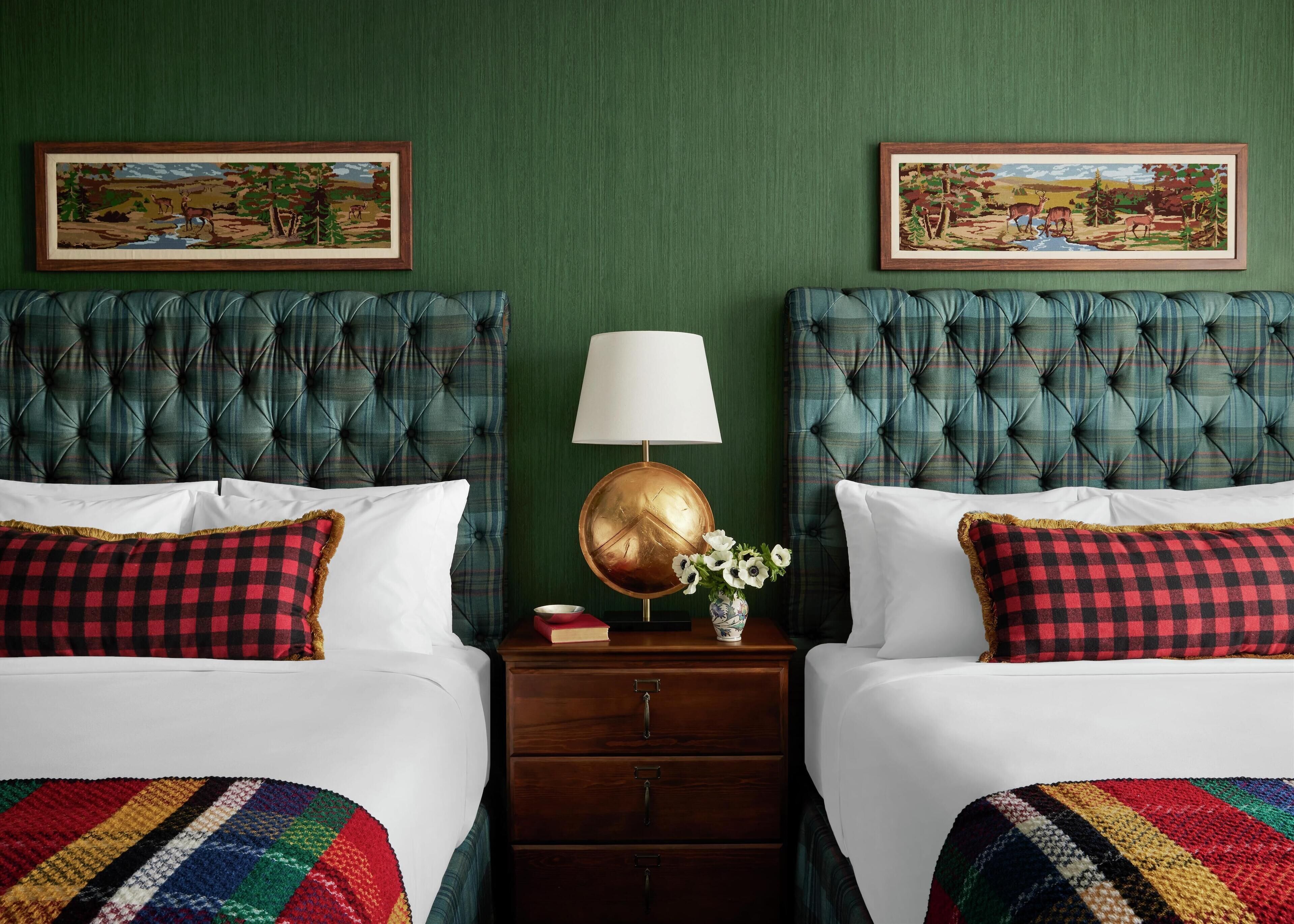 A hotel room with two beds, green walls, and two framed landscape paintings.