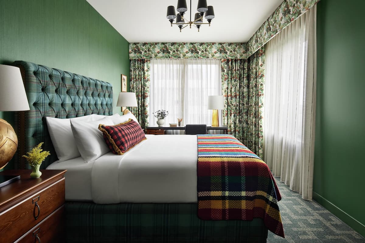 Une chambre d’hôtel avec un grand lit, des murs verts, un lustre et des rideaux à motifs floraux.