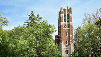 A tall brick tower with a clock, surrounded by lush green trees and grass.