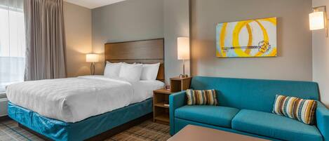 A hotel room with a bed, a sofa, a coffee table, a nightstand, and a wall painting.