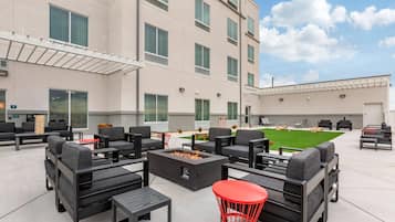 An outdoor seating area with sofas and tables, a fire pit, and a green lawn.