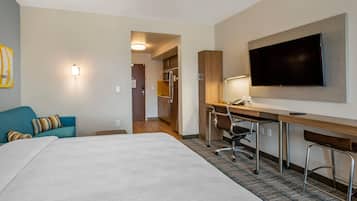 A hotel room with a bed, a desk with a chair, a television, and a kitchenette.