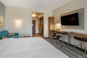 Una habitación de hotel con cama, escritorio con silla, televisión y kitchenette.
