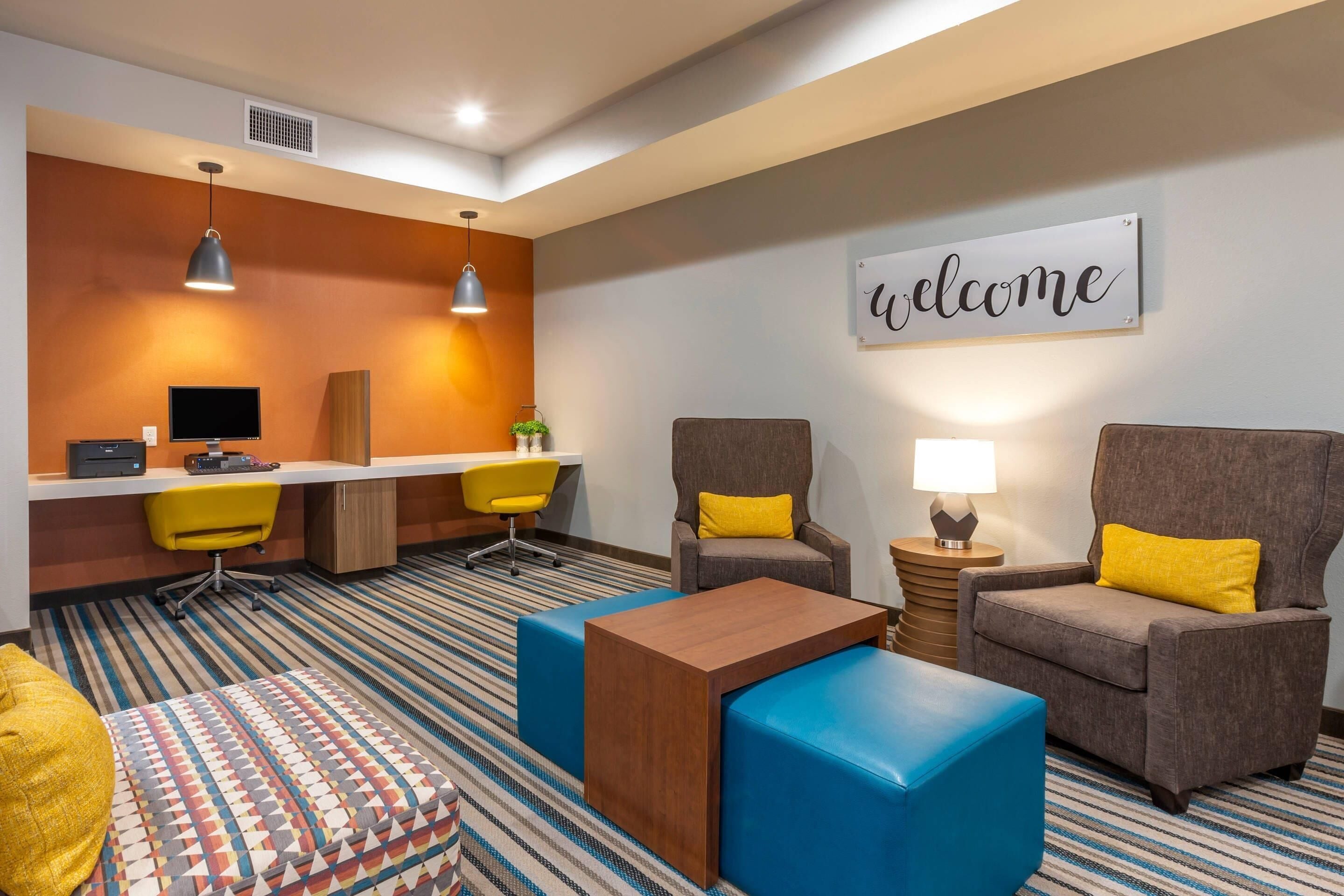 Een hotelkamer met een bureau, twee stoelen, een bank, een salontafel en een kamerbreed tapijt met een patroon.