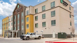 A MainStay Suites hotel building with a modern design, multiple floors, and a parking area with a white pickup truck. - MainStay Suites Carlsbad South (Carlsbad)