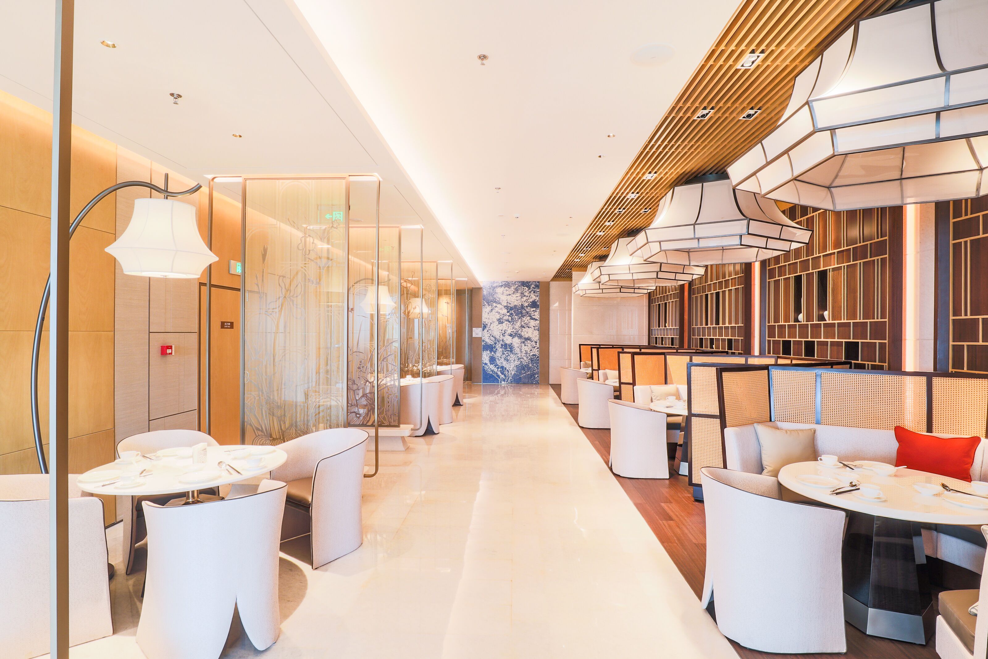 Una hall d'hotel moderna con pareti divisorie in vetro, arredi bianchi e lampade dal design contemporaneo.