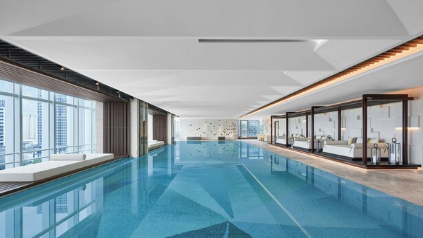 A modern indoor swimming pool with clear glass walls, a geometric floor pattern, and a city view. - Sheraton Guangzhou Panyu (Guangzhou)
