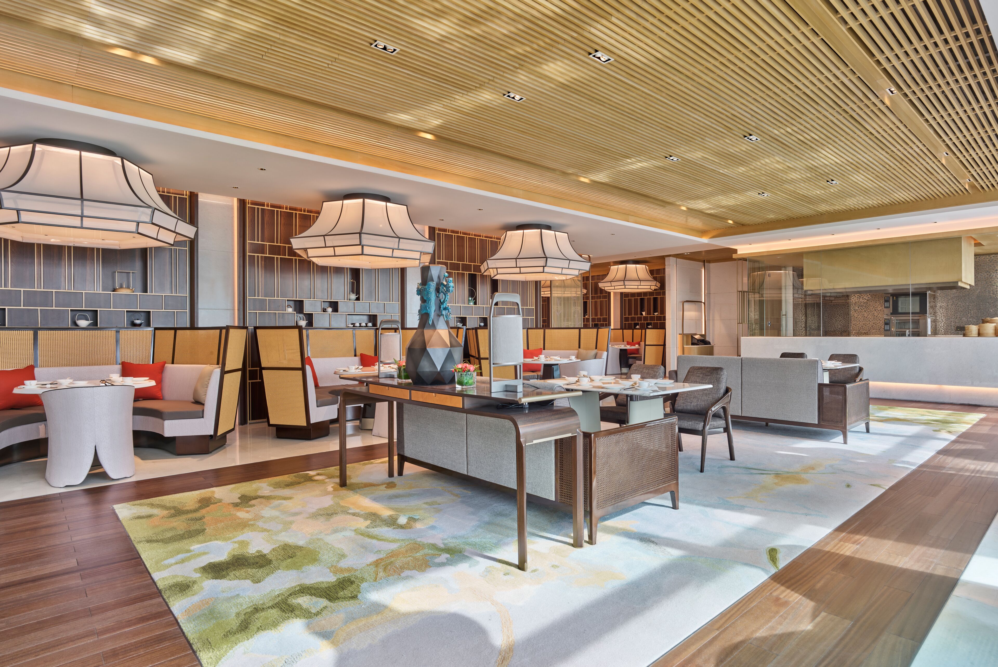 A modern hotel lobby with a central seating area, a kitchen, and a bar.