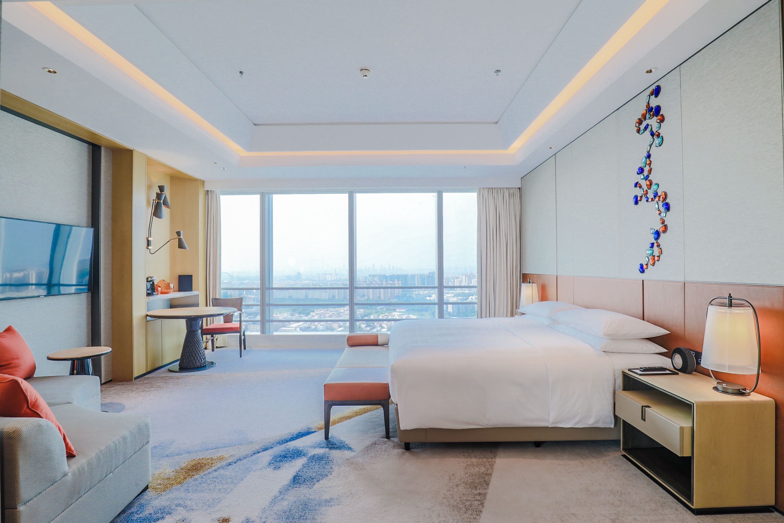 Ein modernes Hotelzimmer mit einem großen Bett, einem Schreibtisch, einem Fernseher und Blick auf die Stadt.