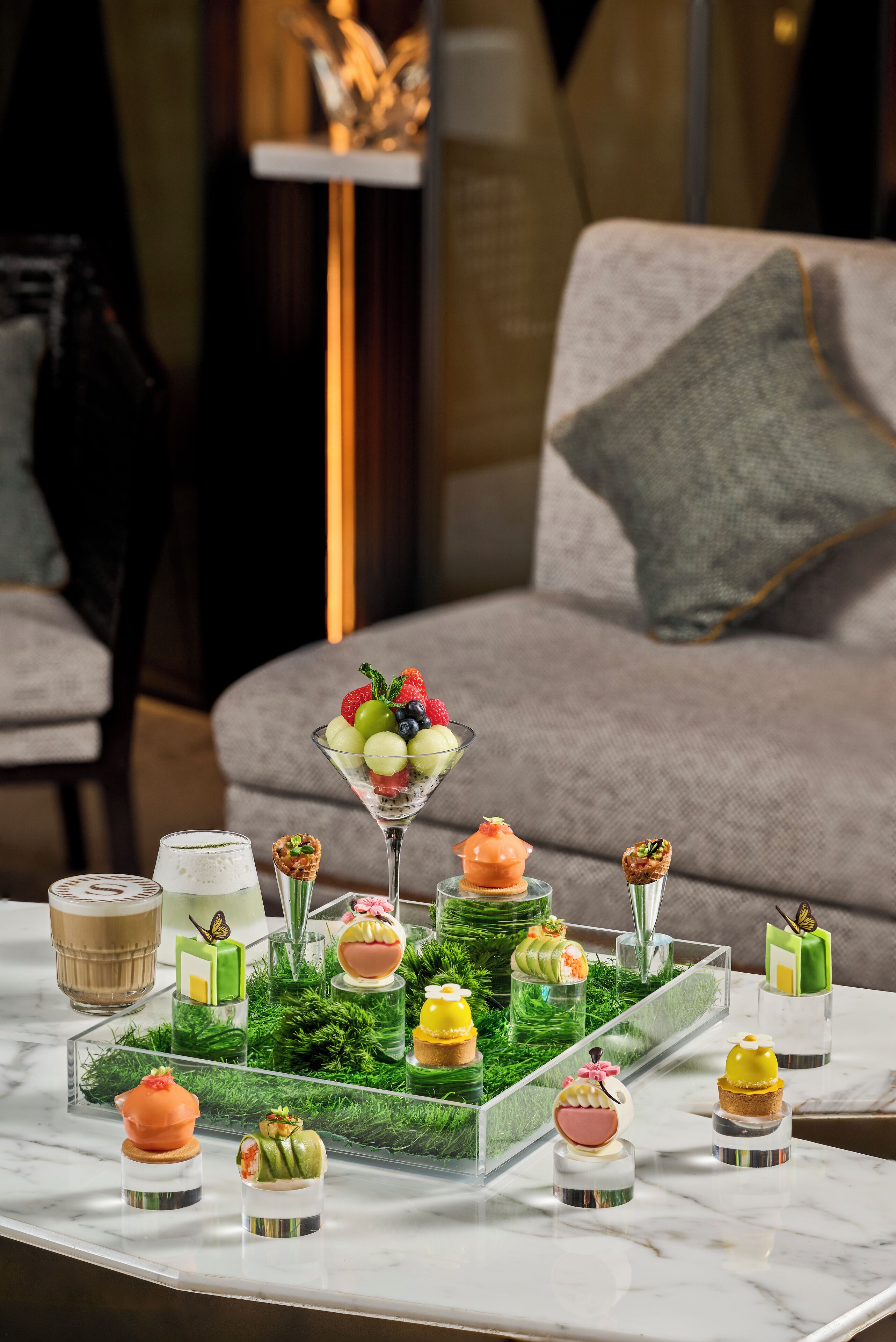 Ett bord med efterrätter uppställt på ett marmorbord i ett rum med en grå soffa och en lampa i bakgrunden.