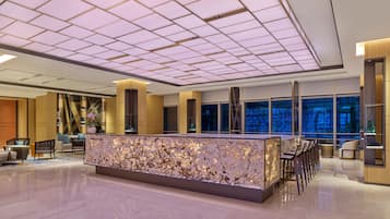 A modern lobby with a central reception desk, seating area, and large windows offering a view of the cityscape.
