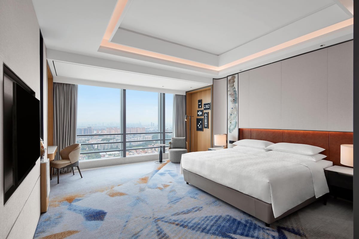 A hotel room with a large bed, a TV, a desk, and a view of the city.