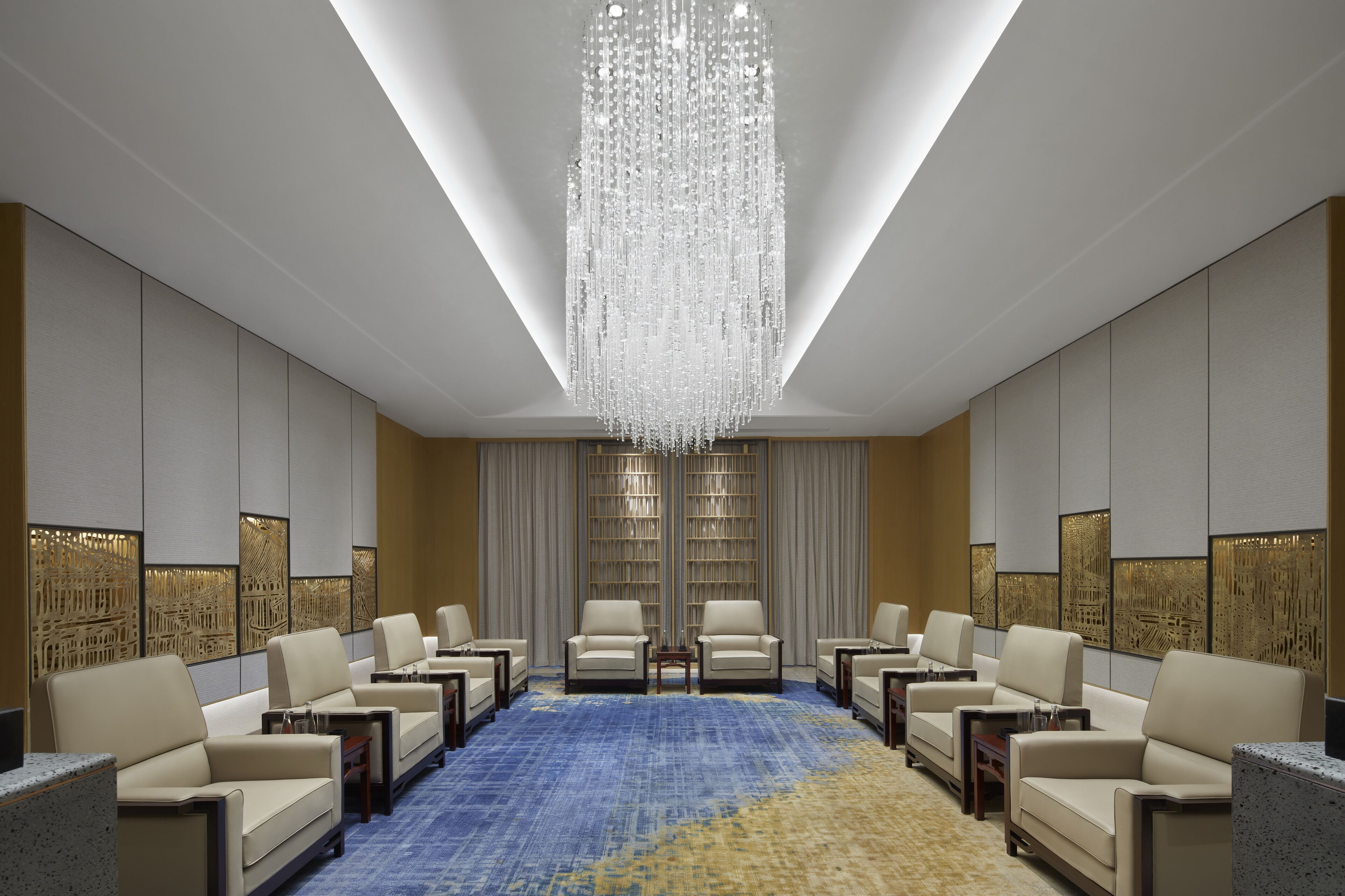 A spacious conference room with a large chandelier, multiple seating arrangements, and a patterned carpet.