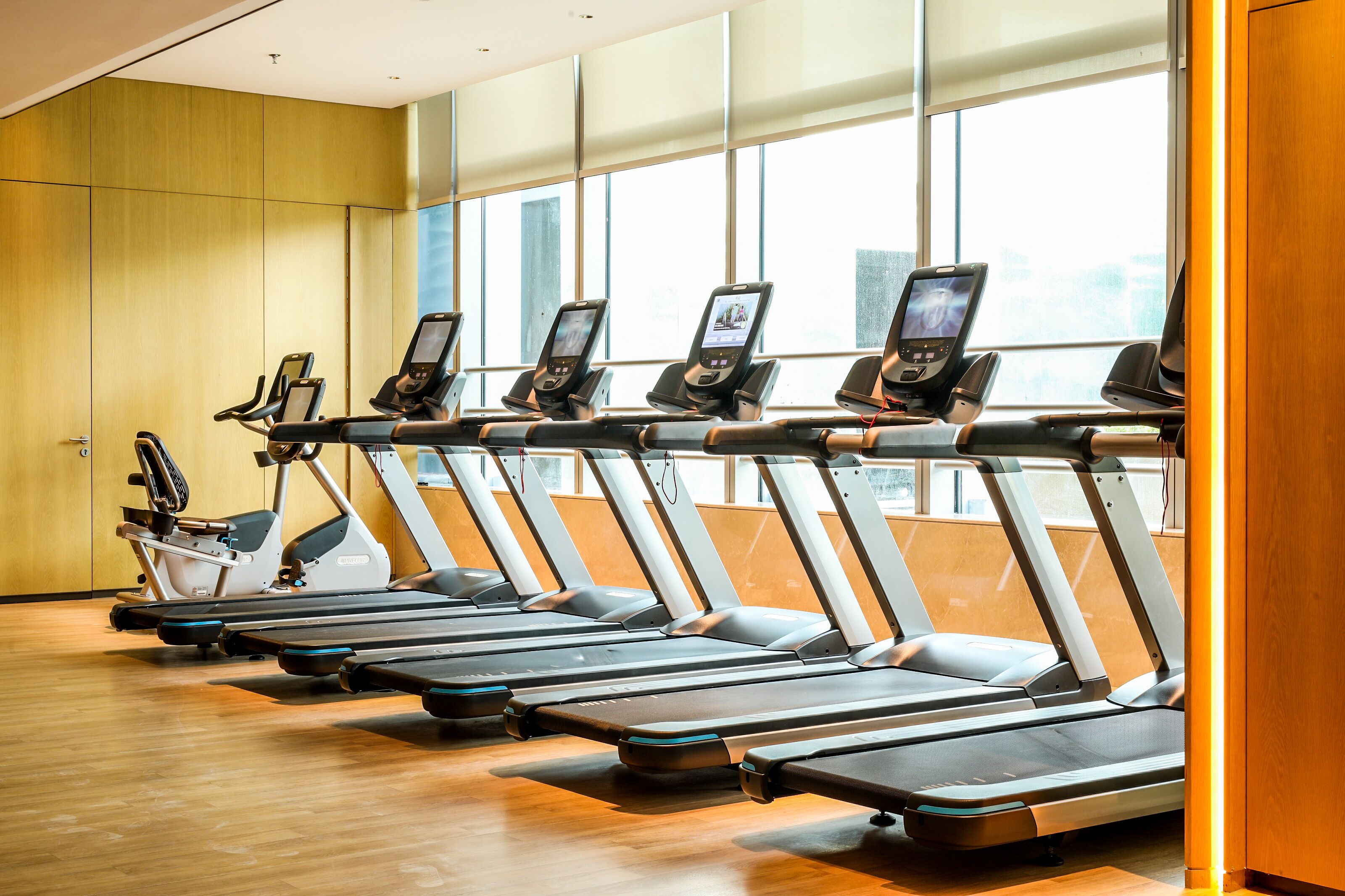 Une rangée de tapis de course dans une salle de sport dotée de grandes fenêtres et de murs en bois.
