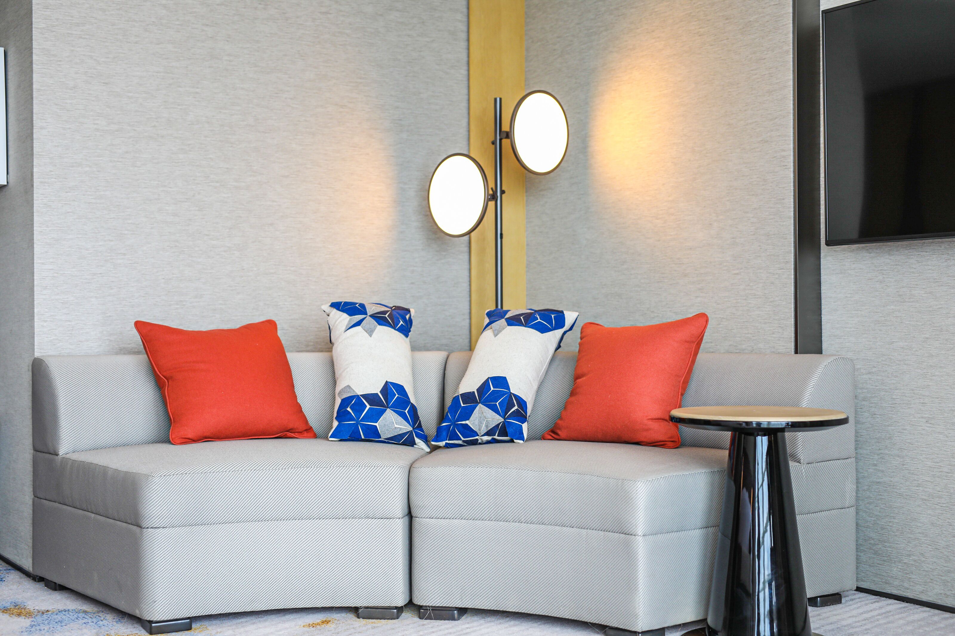 A modern living room with a grey sofa, two round wall-mounted lights, and a small round table.