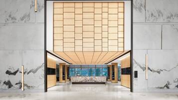 A modern lobby with a reception desk, marble walls, and a large wooden panel ceiling.