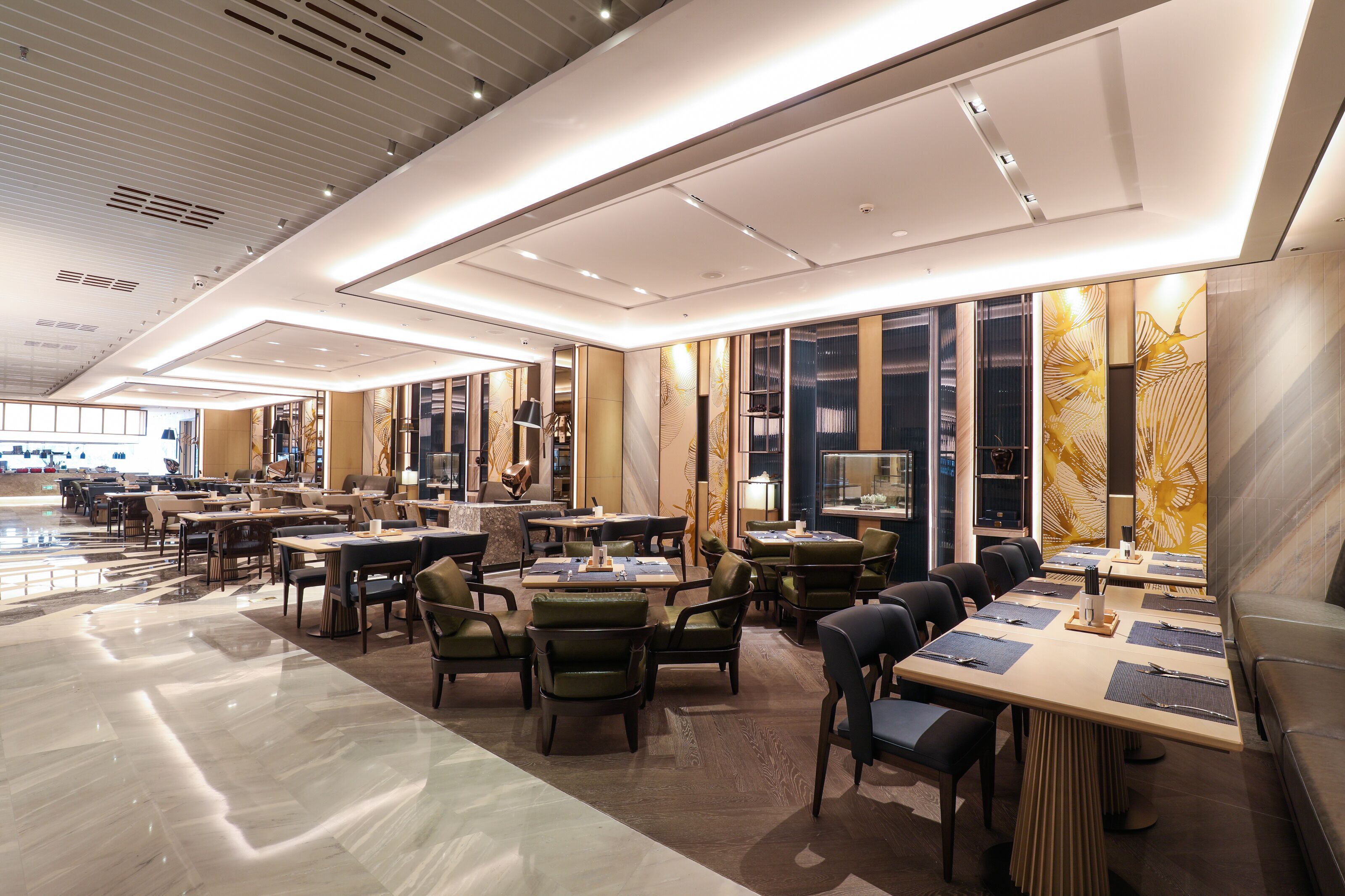 A spacious hotel lobby with multiple seating areas, including tables and chairs, and a large decorative wall with a floral pattern.