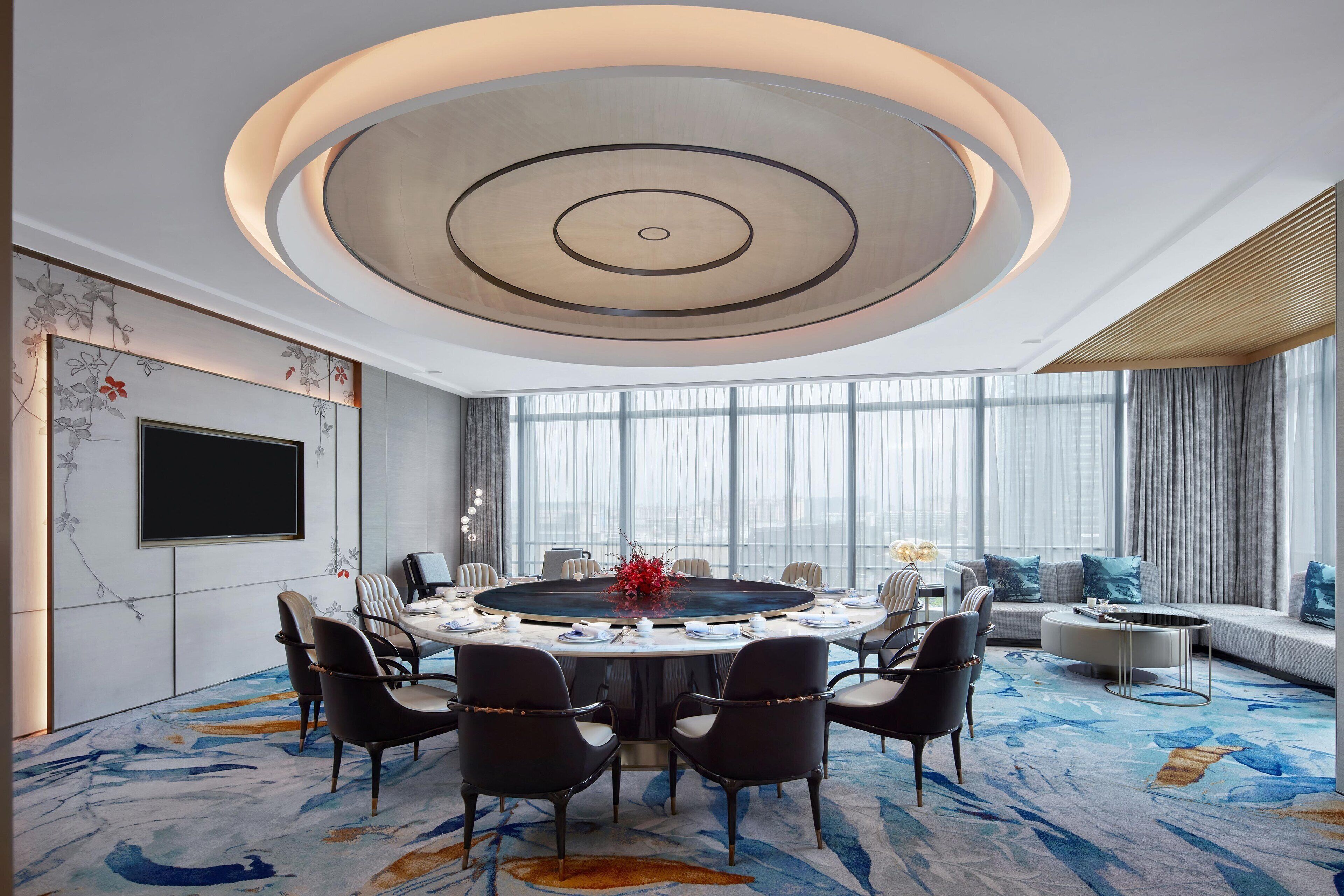 A modern conference room with a round table, chairs, and a large screen.