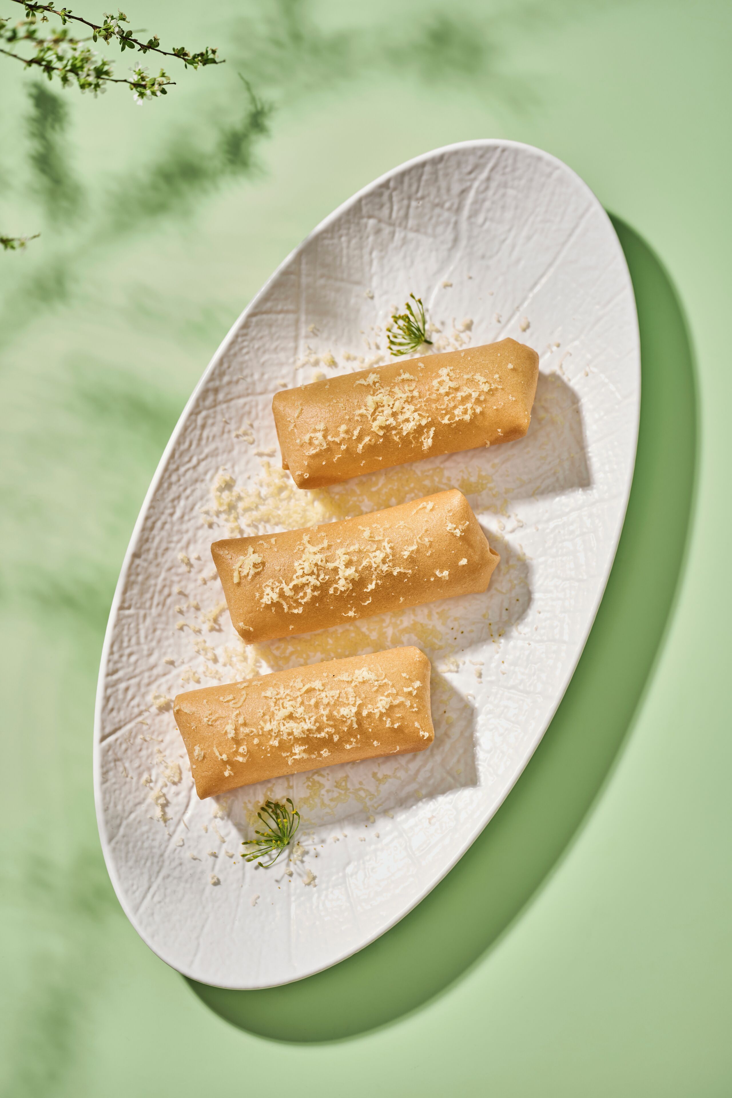 Three spring rolls on a textured white plate with a green background.