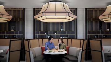 A modern dining area with a round table, two cushioned booths, and a large pendant light.