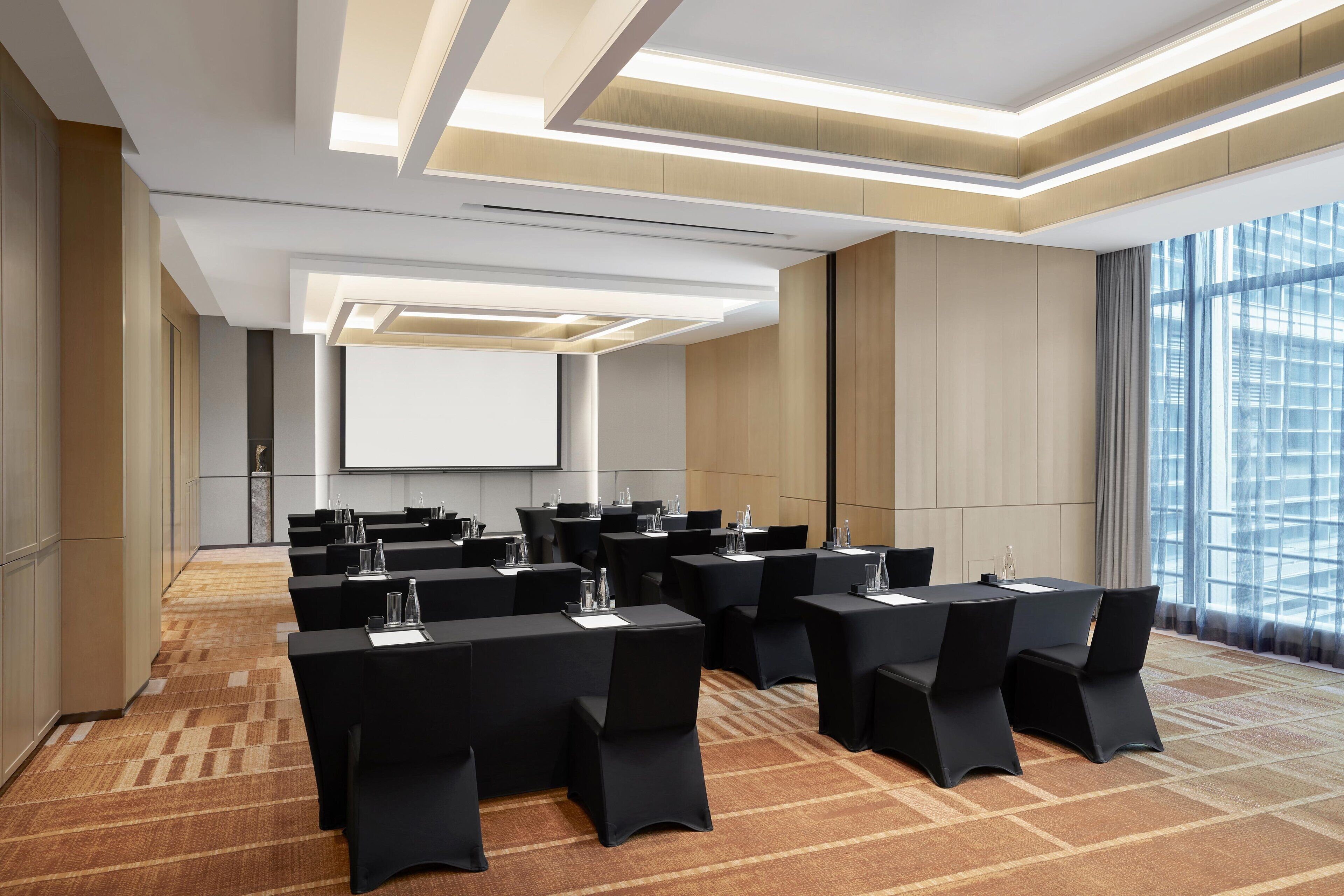 A conference room with multiple tables and chairs, a projector screen, and large windows.