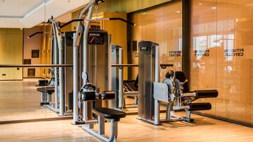 Un gimnasio moderno con diferentes máquinas de ejercicio, un espejo grande y suelo de madera.