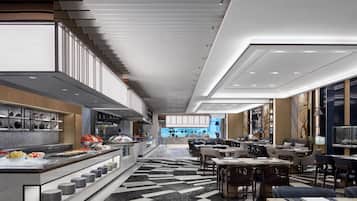 En modern hotellobby med ett område för buffé, sittgrupper och utsikt över stadsbilden.