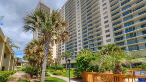 A high-rise hotel with multiple balconies, surrounded by lush greenery and palm trees.