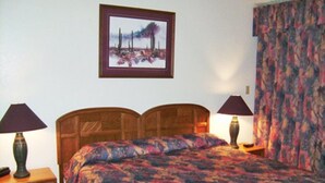 A bedroom with a wooden bed, two bedside tables with lamps, a nightstand, and a framed picture on the wall.