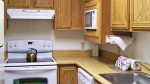 A kitchen with wooden cabinets, a stove, a microwave, and a sink.