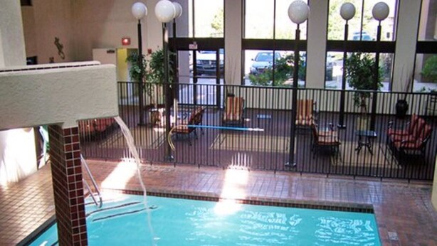 An indoor swimming pool with a tiled floor, a metal fence, and a bench area with chairs.