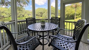 A covered outdoor seating area with a round table and four chairs, overlooking a natural landscape. - Beautiful Furnishings! Great Location! (Myrtle Beach)