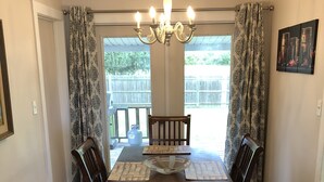Un comedor con una mesa de madera, cuatro sillas, una araña y cortinas con estampado.