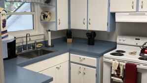 Una cocina con armarios blancos, un fregadero, una estufa y una ventana con un reloj.